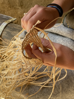 Hände flechten ein Geflecht aus Naturfasern auf einem grauen Untergrund