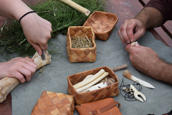 Zwei Hände bearbeiten Knochenstücke auf einem Tisch mit geflochtenen Körben
